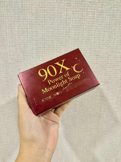 Hand holding a red box of '90X Power of Moonlight Soap' with gold text against a beige background