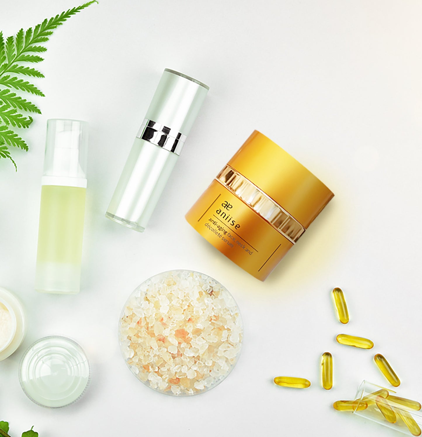Cosmetic products including a gold jar, bottles, and capsules on a light background with greenery.